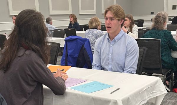 Student sitting at a table, speaking to a person