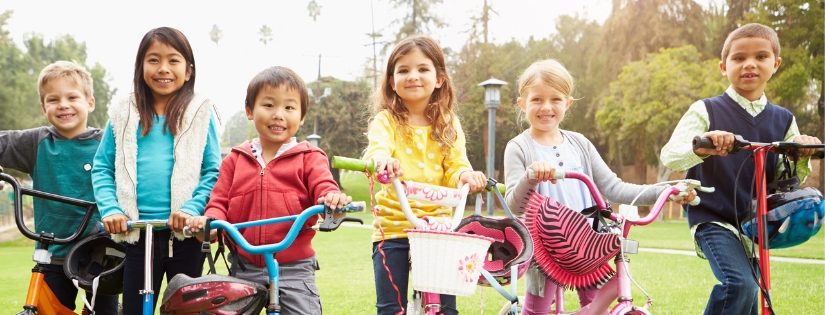 Children smiling on bikes and scooters