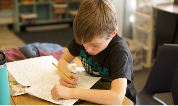 Student writing with a pencil and sitting at a desk